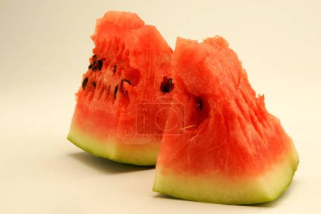 Fruits ; Two pieces of watermelon showing red watery pulp against white background ; Pune; Maharashtra; India