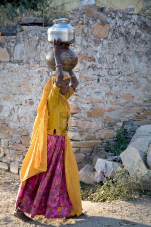 Foto de Mujer rural que lleva ollas de agua en la cabeza; pueblo semiurbano Dilwara; Udaipur; Rajastán; India - Imagen libre de derechos
