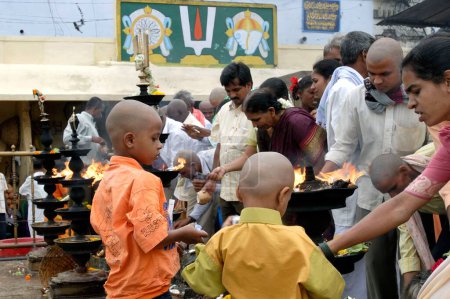 Foto de Devotos adorando y ofreciendo coco; alcanfor y flores al Señor Venkateshwara (Balaji) frente a las enormes lámparas de aceite en el templo Tirumala; Tirupati, Andhra Pradesh, India - Imagen libre de derechos