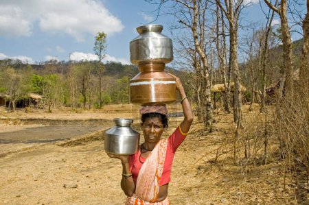 Photo for Tribal woman carrying water pots on head and hand large distance covered to fetch water ; Thane district near Mumbai Bombay ; Maharashtra ; India - Royalty Free Image