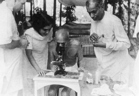 Foto de Mahatma Gandhi examinando células de anquilostomas a través de un microscopio en Juhu Beach. Mumbai. Mayo de 1944. Sushila Nayar. La Dra. Dinshah Mehta y la Dra. Gajjar. India - Imagen libre de derechos