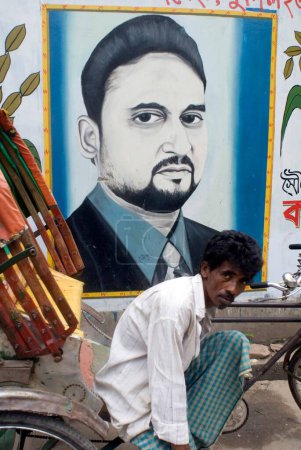 Foto de Ciclo Rickshaw Jinete sentado cerca de la pared Pintura de graffiti político; Dhaka; Bangladesh - Imagen libre de derechos