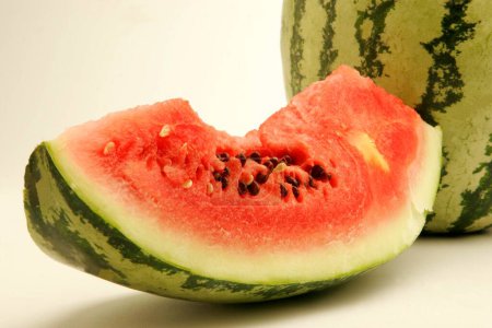 Fruits ; Cut piece of watermelon showing red watery pulp with black seeds against  one on white background ; Pune ; Maharashtra ; India