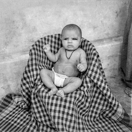 Photo for Old vintage 1900s black and white studio portrait of Indian baby boy child wearing nappy diaper sitting stool India 1940s - Royalty Free Image