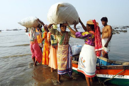 Foto de Pescadoras indias del sur de Asia llevando cargas de pescado en sus cabezas que fueron transportadas en pequeñas embarcaciones para la venta en Uttan Beach; cerca de Bombay ahora Mumbai; Maharashtra; India - Imagen libre de derechos
