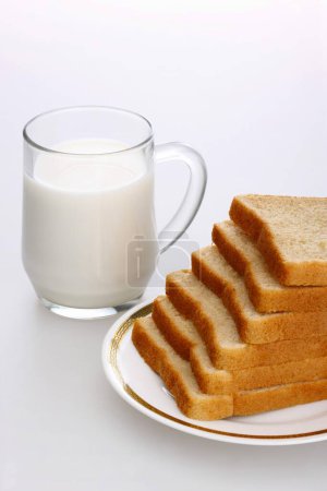 Rebanadas de pan moreno en un plato con una taza de leche
