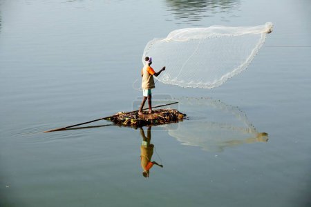 Photo for A fisherman from the Haripur village on a makeshift boat throwing his net to catch fish in Krishna River in Sangli district ; Maharashtra ; India - Royalty Free Image