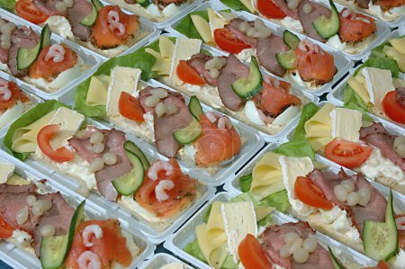 Photo for Food , Landgang open sandwich with bread from right starting with cheese , brei cheese , potatoes salad , roast beef , marinated schalloten onions , majonnas topped with prawns and smoked salmon Garnished with salad leaves , tomatoes and twist of cuc - Royalty Free Image