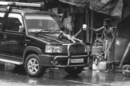 Photo for Man and naked boy washing car in Byculla slum. N M Joshi Road. Bombay Mumbai. Maharashtra. India - Royalty Free Image