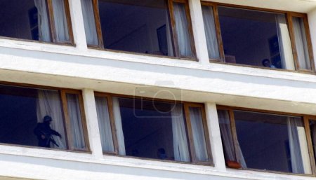 Téléchargez les photos : Garde de sécurité nationale NSG commando ouvrant le rideau pour indiquer que la chambre est à l'abri des terroristes moudjahidines Deccan à Oberoi (hôtel Trident) Nariman Point ; Bombay Mumbai ; Maharashtra ; Inde 27 novembre 2008 - en image libre de droit