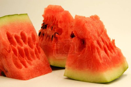 Fruits ; Three quarter pieces of watermelon showing red watery pulp against white background ; Pune; Maharashtra; India