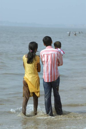 Photo for Couple with child in arm enjoying in water of Arabian sea at Juhu beach, Bombay Mumbai, Maharashtra, India - Royalty Free Image