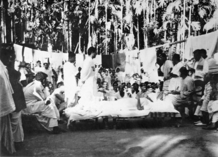 Téléchargez les photos : Mahatma Gandhi, tout en se reposant, parler aux gens dans les émeutes du Bengale oriental Noakhali entre hindous et musulmans - en image libre de droit