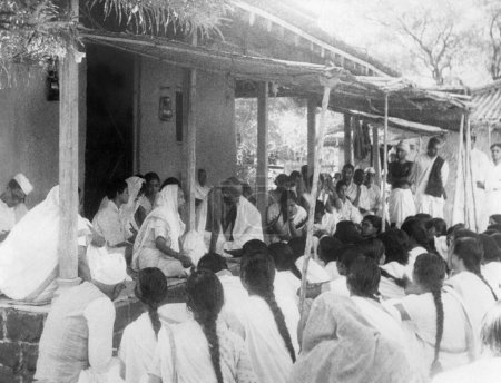Téléchargez les photos : Kasturba Gandhi et Mahatma Gandhi assis avec les filles de Mahila Ashram Wardha à l'occasion de l'anniversaire de la roue tournante Charkha Jayanti à l'ashram de Sevagram, 1940 - en image libre de droit