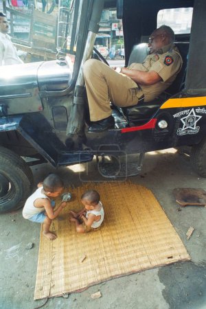 Téléchargez les photos : Enfants de la rue jouant à la jeep de la police de Mumbai un constable se reposant à l'intérieur - en image libre de droit