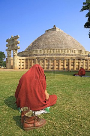 Foto de Monje budista leyendo escrituras frente a la Stupa 1 construida por el rey Ashok, Sanchi, Madhya Pradesh, India - Imagen libre de derechos