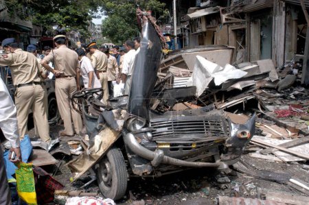 Photo for Policemen inspecting site of bomb blast also remain of taxi at Zaveri Bazaar in busy Kalbadevi area; Bombay Mumbai, Maharashtra, India August 26th 2003 - Royalty Free Image