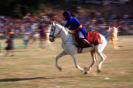 Foto de Nihang o guerrero sij llevando lanza realizando acrobacias a caballo durante el festival Hola Mohalla en el sahib de Anandpur en el distrito de Rupnagar; Punjab; India - Imagen libre de derechos