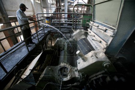 Téléchargez les photos : Un travailleur saupoudrant de l'eau de vapeur sur la machine à l'usine de sucre de Sangli, Maharashtra, Inde - en image libre de droit