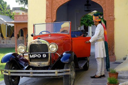 Foto de Portero que abre la puerta del coche de época en Rawla Jojwar Heritage Hotel; Marwar; Rajasthan; India PRMR746B - Imagen libre de derechos
