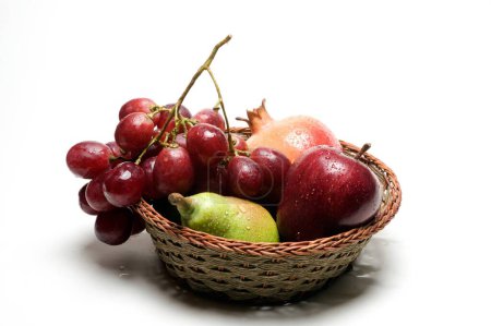 Foto de Frutas, gotas de agua sobre manzana, granada, pera y uvas en canasta de madera sobre fondo blanco - Imagen libre de derechos