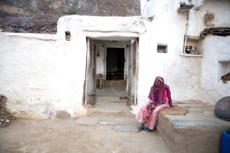 Foto de Anciana sentada fuera de la casa de barro esperando; pueblo Dilwara; Udaipur; Rajastán; India - Imagen libre de derechos