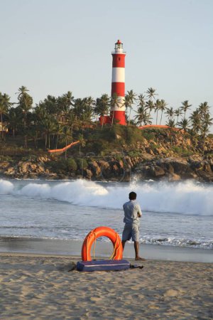 Photo for Kovalam beach and light house ; orange life guard ring with life guard watching waves ; Thiruvananthapuram District ; Kerala ; India - Royalty Free Image