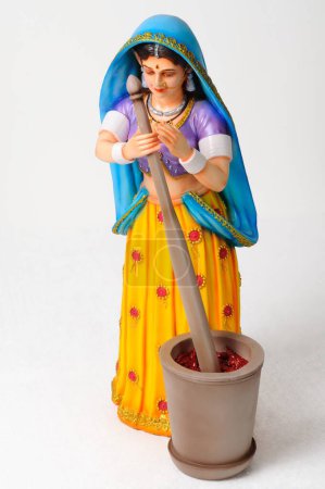 Clay figurine , statue of rajasthani woman pounding spices red chillies in mortar with pestle