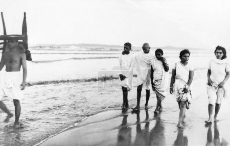 Foto de Mahatma Gandhi y otros caminando Juhu Beach, Mumbai, mayo 1944, Kanu Gandhi, llevando una silla en su cabeza, Sushila Nayar, India - Imagen libre de derechos