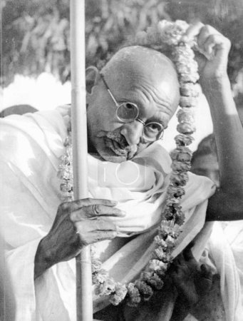Téléchargez les photos : Mahatma Gandhi enlevant un "mala des fleurs", un signe de salutation qu'il avait reçu en route vers Noakhali, Bengale occidental, Inde, novembre 1946 - en image libre de droit