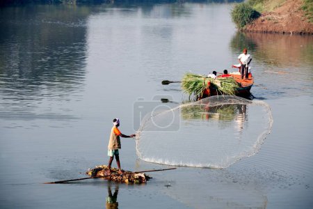 Téléchargez les photos : Un pêcheur du village de Haripur sur un bateau de fortune jetant son filet pour attraper du poisson dans la rivière Krishna dans le district de Sangli ; Maharashtra ; Inde - en image libre de droit