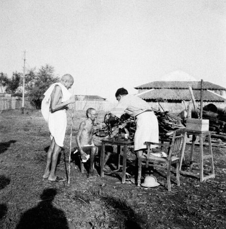 Téléchargez les photos : Mahatma Gandhi observant un patient lépreux Parchure Shastri examiné par un médecin externe à l'Ashram de Sevagram, 1940 - en image libre de droit