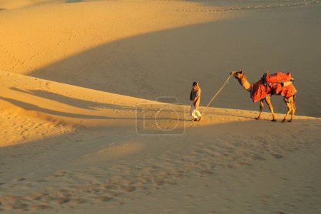 Téléchargez les photos : Chameau avec propriétaire marchant dans les dunes de sable doux à Sam ; Jaisalmer ; Rajasthan ; Inde - en image libre de droit