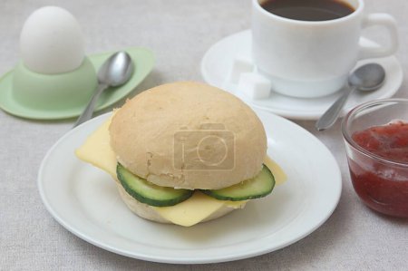 Foto de Comida, Rollo de pan con queso y pepino, huevo hervido en el titular del huevo y cuchara, taza de café, terrones de azúcar, mermelada de fresa - Imagen libre de derechos