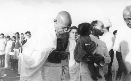 Photo for Mahatma Gandhi with Sushila Nayar b c and Pyarelal Nayar, who carries his younger brothers Mohans daughter Nandini at Sevagram Ashram, August 1944 - Royalty Free Image