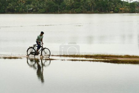 Photo for Man on bicycle going through road covered with water due to monsoon, Alappuzha Alleppey, Kerala, India - Royalty Free Image