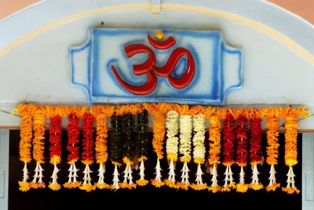 OM en color rojo; creación cósmica; palabra santa de religión hindú con guirnalda colorida de diferentes flores en la entrada del templo Shri Dasabhuj Lakshmi Ganesh en Hedvi; región de Konkan; Taluka Guhagar; Distrito Ratnagiri; Maharashtra; India