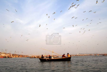 Téléchargez les photos : Les dévots sont assis dans un bateau arrivant au confluent du Gange ; rivières Yamuna et Saraswati pour prendre un bain sacré pendant Ardh Kumbh Mela, Allahabad, Uttar Pradesh ; Inde - en image libre de droit