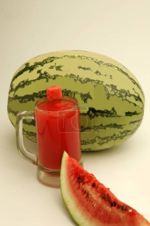 Fruits ; One full watermelon with light and dark green stripes and one cut slice showing red watery pulp and black seeds with glass of melon juice  ; Pune ;  Maharashtra ; India