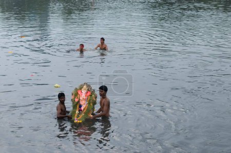 Téléchargez les photos : Une petite idole de Lord Ganesh prise par deux hommes pour immersion dans l'eau Pune Inde Asie - en image libre de droit