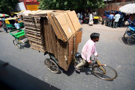 Foto de Un rickshaw de triciclo cargado con cajas de cartón desmontadas siendo jalado por una walla de rickshaw cerca del fuerte rojo en la vieja Delhi; India - Imagen libre de derechos