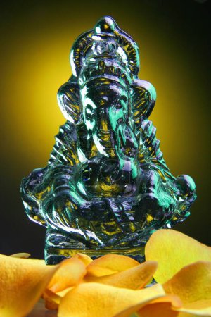 Téléchargez les photos : Table Top Studio shot of Glass Idol of Lord Ganesh Ganapati, Éléphant dirigé Dieu avec des pétales de rose de couleur jaune - en image libre de droit