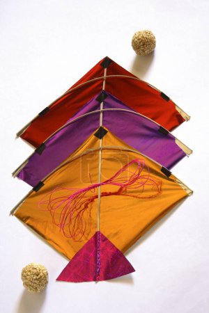 Colourful kites thread and sweet tilgur or til gul sesame laddoos for Makara Sankranti festival on white background