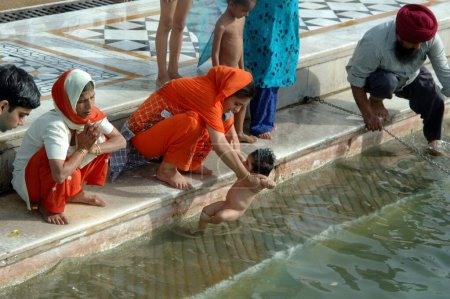 Téléchargez les photos : Les dévots sikhs prennent un bain sacré dans le sarovar Amrit le lac de nectar, temple d'or, Amritsar, Punjab, Inde - en image libre de droit