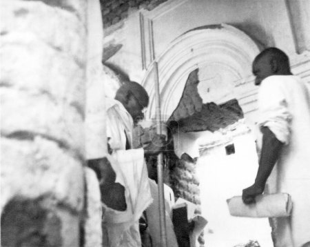 Téléchargez les photos : Mahatma Gandhi et d'autres entrent dans une maison endommagée par les émeutes entre hindous et musulmans au Noakhali Bengale oriental - en image libre de droit