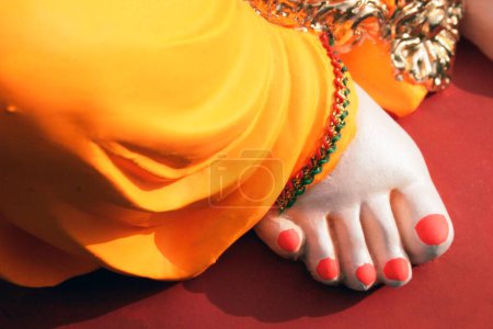 Téléchargez les photos : Le pied droit avec un vêtement de couleur orange appelé Pitamber et des ongles peints de l'idole de Lord Ganesh ; Pune ; Maharashtra ; Inde - en image libre de droit
