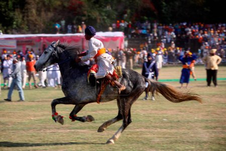 Téléchargez les photos : Guerrier nihang ou sikh effectuant des cascades à cheval lors de la célébration Hola Mohalla à Anandpur sahib dans le district de Rupnagar, Punjab, Inde - en image libre de droit