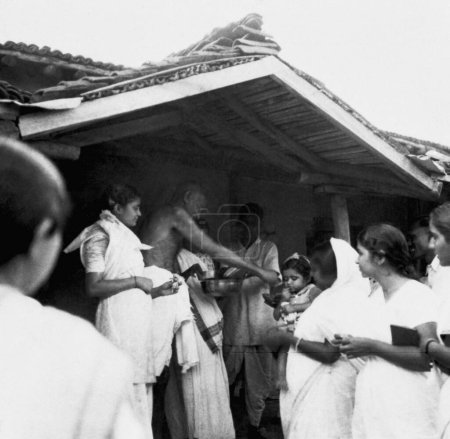 Téléchargez les photos : Mahatma Gandhi donnant des bonbons à la fille d'Uma Om Agarwal la plus jeune fille de Jamnalal Bajaj à l'Ashram de Sevagram, 1942 - en image libre de droit