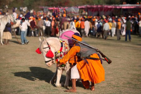 Foto de Nihang o Sikh guerrero con rifle y caballo durante la celebración Hola Mohalla en Anandpur sahib en el distrito de Rupnagar, Punjab, India - Imagen libre de derechos