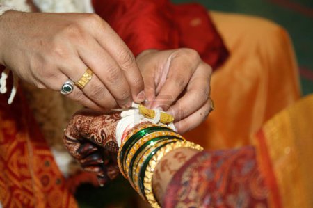 Photo for Bridegroom tying kankan or halkund with thread on wrist of bride performing ritual vidhi in maharashtrian wedding ceremony - Royalty Free Image